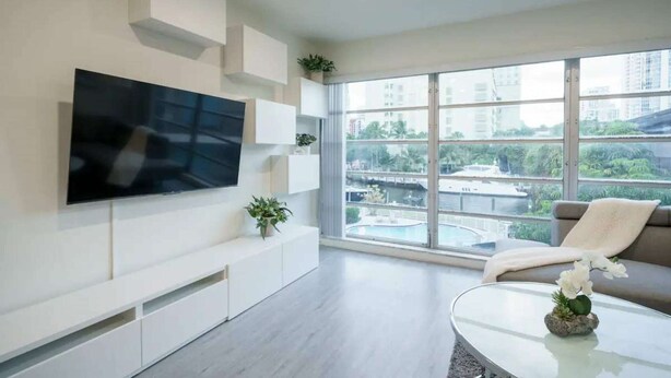 Een moderne woonkamer met een flatscreen televisie, inbouwkasten, een bank, een salontafel en een groot raam met uitzicht op de stad.