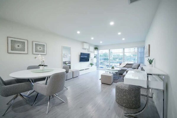A modern living room with a dining area, large windows, and a flat-screen TV.