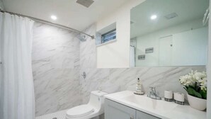 Een badkamer met toilet, douche, wastafel en spiegel.