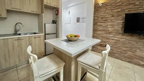 A modern kitchen with wooden cabinets, a white countertop, a built-in refrigerator, and a stone wall with a mounted TV. - 157 LIM - Stay Sunsea Studio (Limassol)