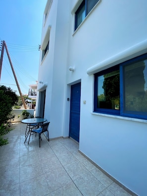 A modern building with a blue door and windows, a tiled patio with a table and chairs, and a visible power line.