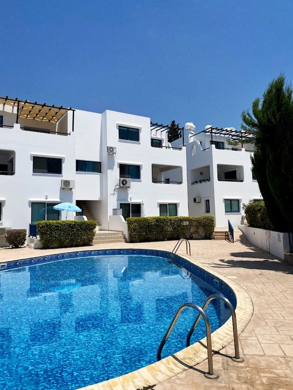 A modern building with a swimming pool, featuring balconies and air conditioning units.