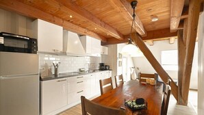 Eine Küche mit weißen Schränken, einer Holzbalkendecke und einem Esstisch mit Stühlen.