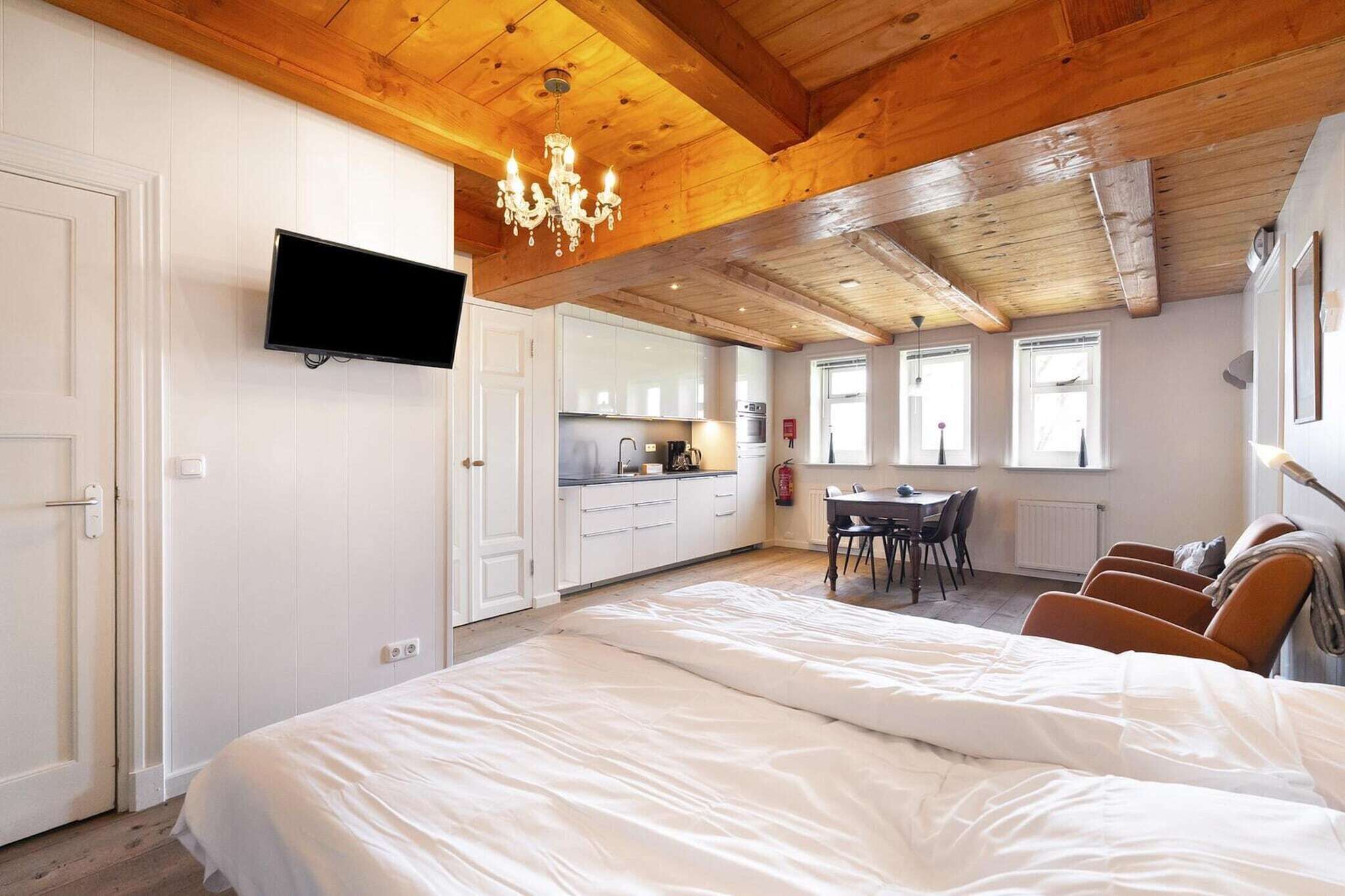 Een slaapkamer met een groot bed, een aan de muur bevestigde televisie, een kroonluchter en een keuken met een eettafel en stoelen.