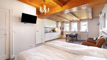 Een slaapkamer met een groot bed, een aan de muur bevestigde televisie, een kroonluchter en een keuken met een eettafel en stoelen.