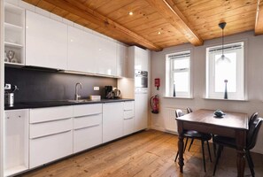A kitchen with white cabinets, a black countertop, a wooden ceiling, and a dining table with chairs.