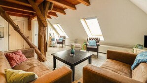 Een loft-achtige woonkamer met zichtbare houten balken, een bank, een bijzettafeltje en uitzicht door dakramen.