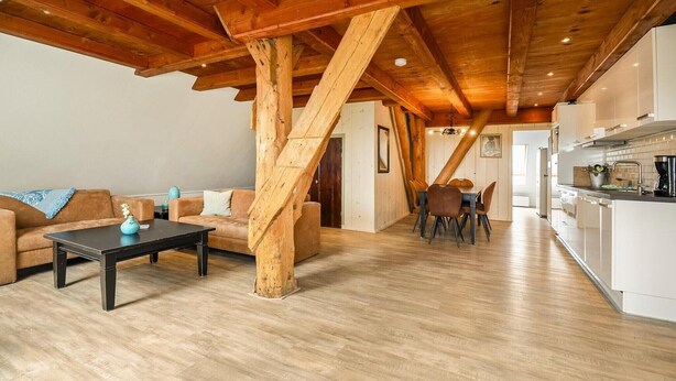 Een ruime woonruimte met een houten plafond, een eettafel met stoelen en een keukenhoek.