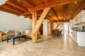 A spacious living area with a wooden ceiling, a dining table with chairs, and a kitchen area.