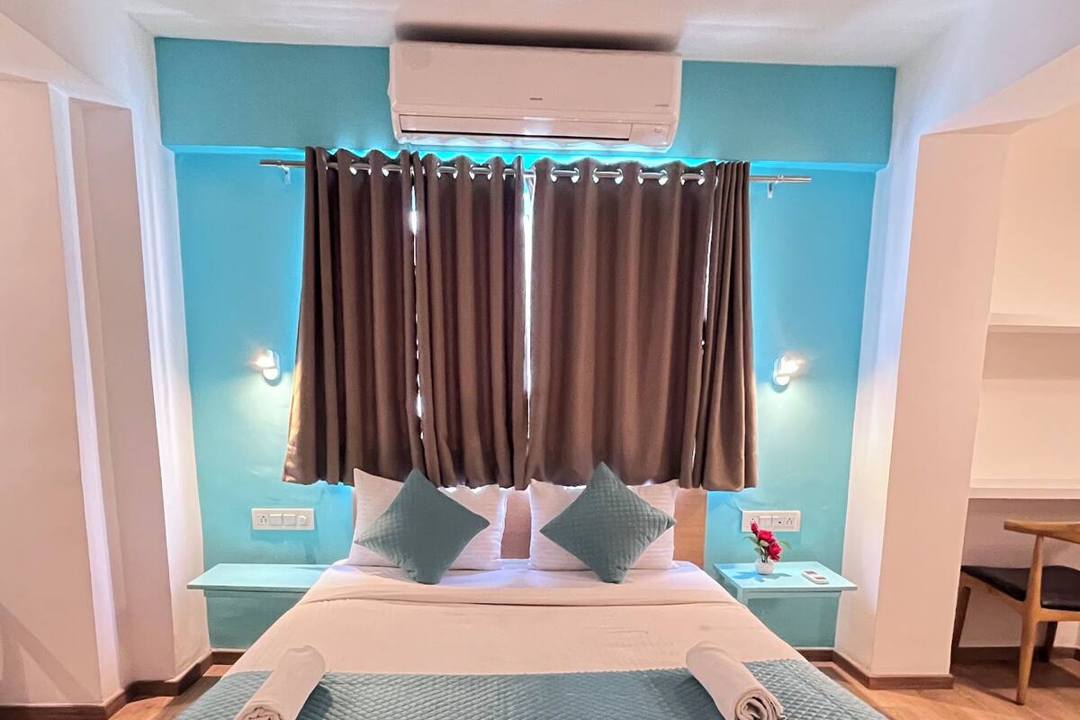 A bedroom with a large bed, a nightstand, a desk, and a window with curtains.