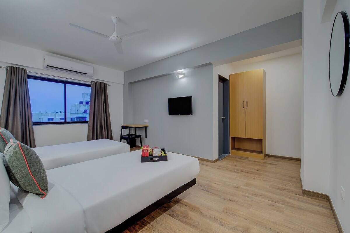 A modern hotel room with two beds, a ceiling fan, a TV, and a view of the cityscape.