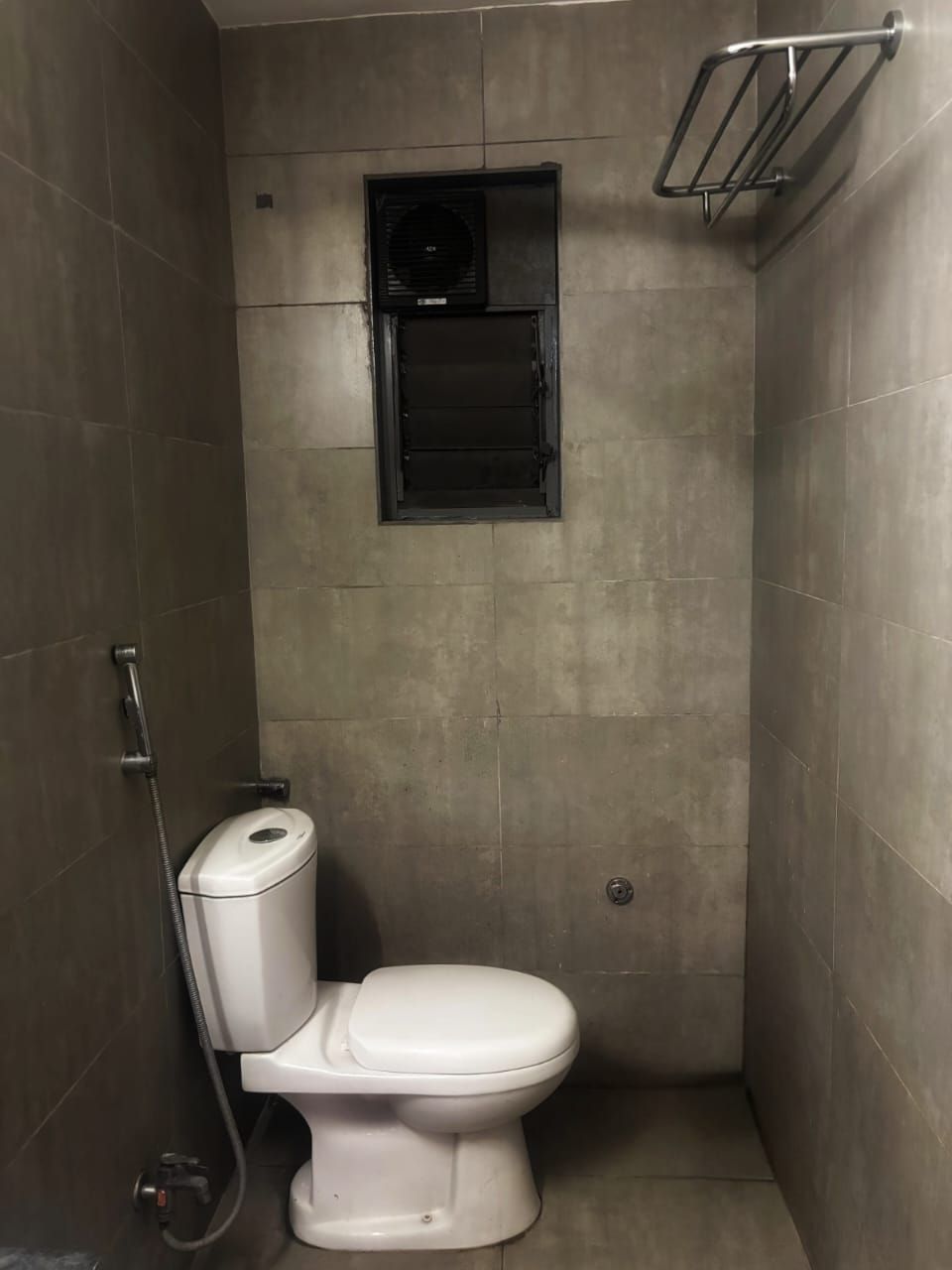 Een kleine betegelde badkamer met toilet, douche en raam.