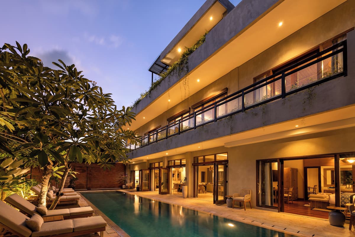 Un edificio moderno de varios pisos con piscina, mobiliario exterior y un balcón con plantas.