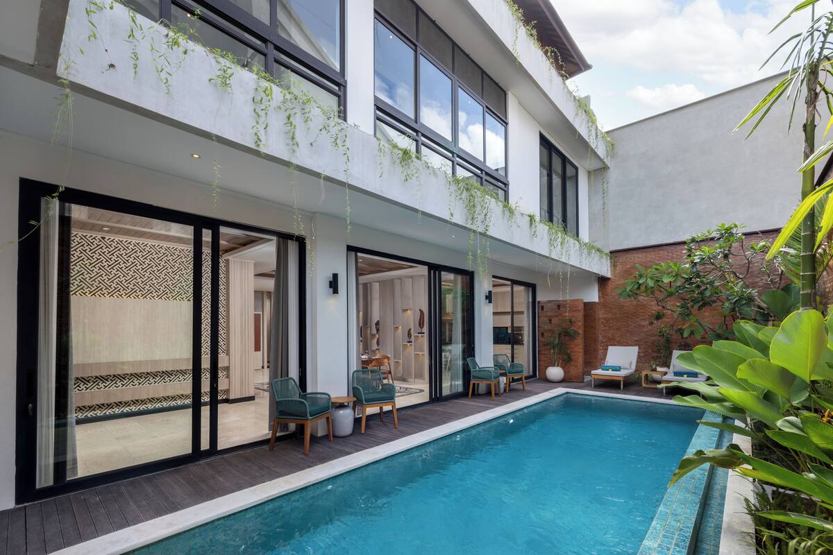 Un edificio moderno con piscina, mobiliario exterior y un patio cubierto.