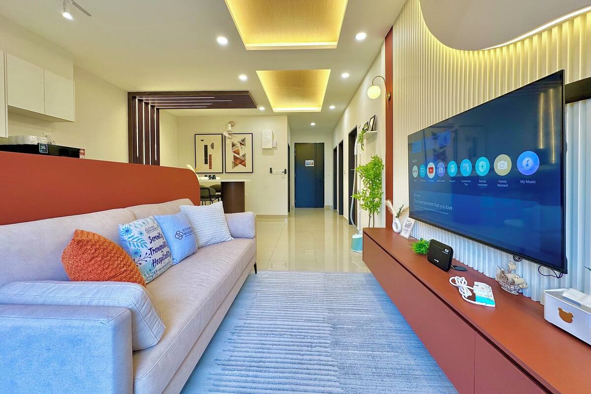 Una sala moderna con televisor de pantalla plana, un sofá con almohadones decorativos y una alfombra azul.