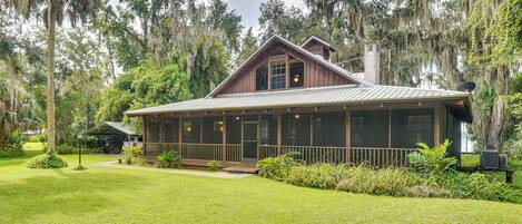 A rustic cabin with a large porch, surrounded by lush greenery and tall trees.