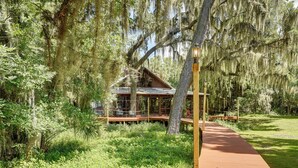 Eine rustikale Holzhütte mit einer Holzterrasse, umgeben von üppigem Grün und Bäumen mit hängenden Moosen.