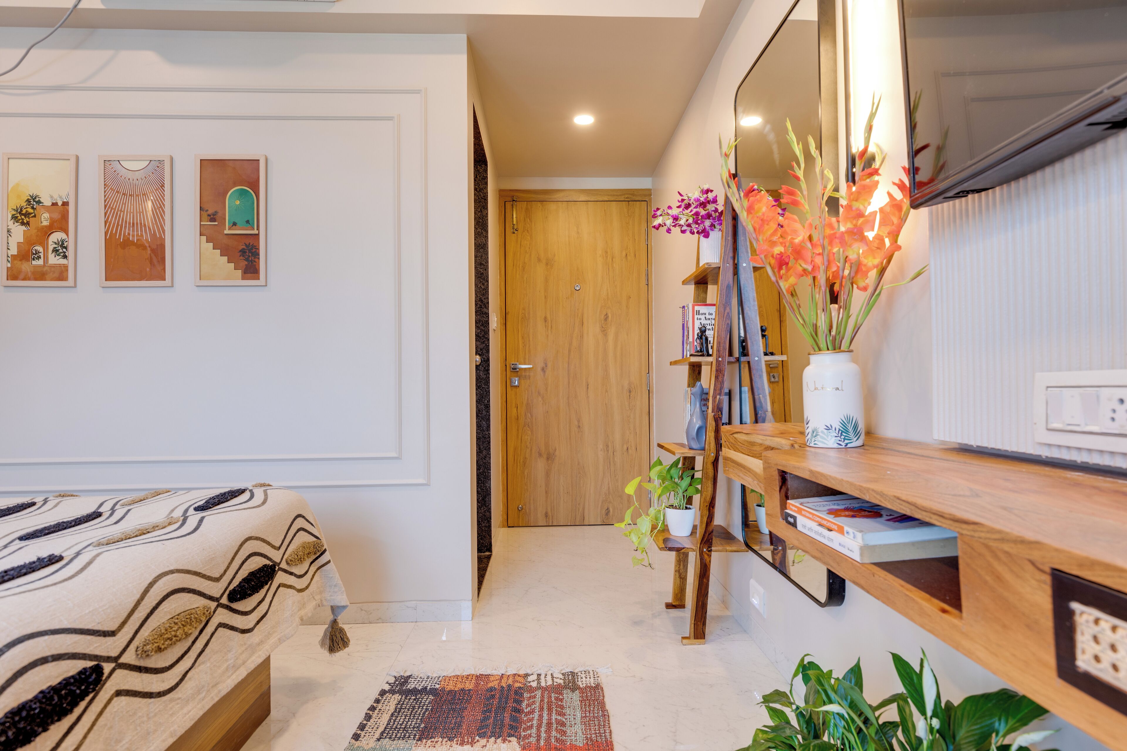 A bedroom with a bed, a wooden bedside table, a mirror, and a wall with three framed artworks.