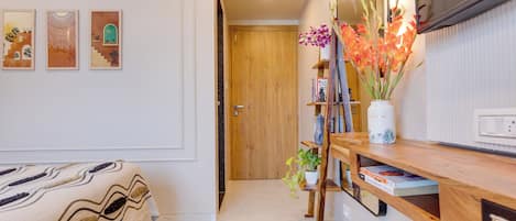 A bedroom with a bed, a wooden bedside table, a mirror, and a wall with three framed artworks.