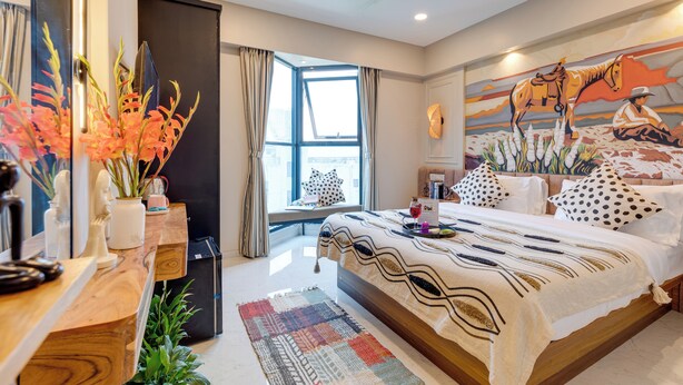 Un dormitorio moderno con una cama grande, una ventana con cortinas, un ventilador de techo y un mural en la pared.