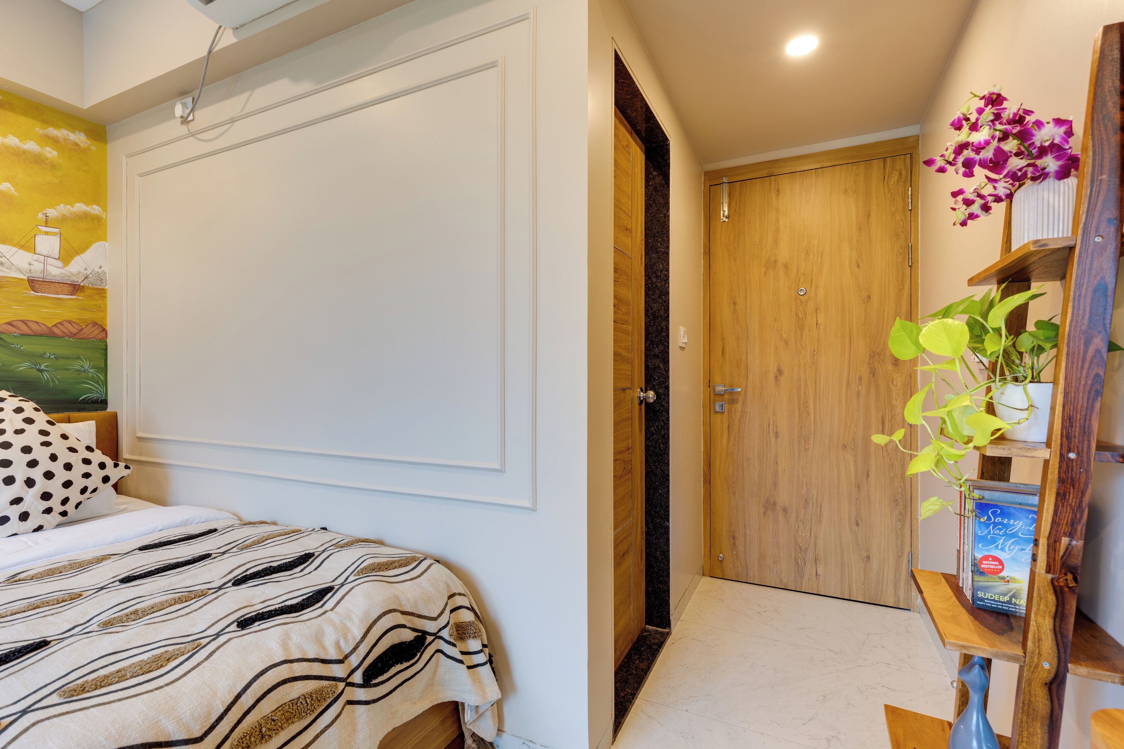 A bedroom with a bed, a wooden door, and a shelf with a book and a plant.
