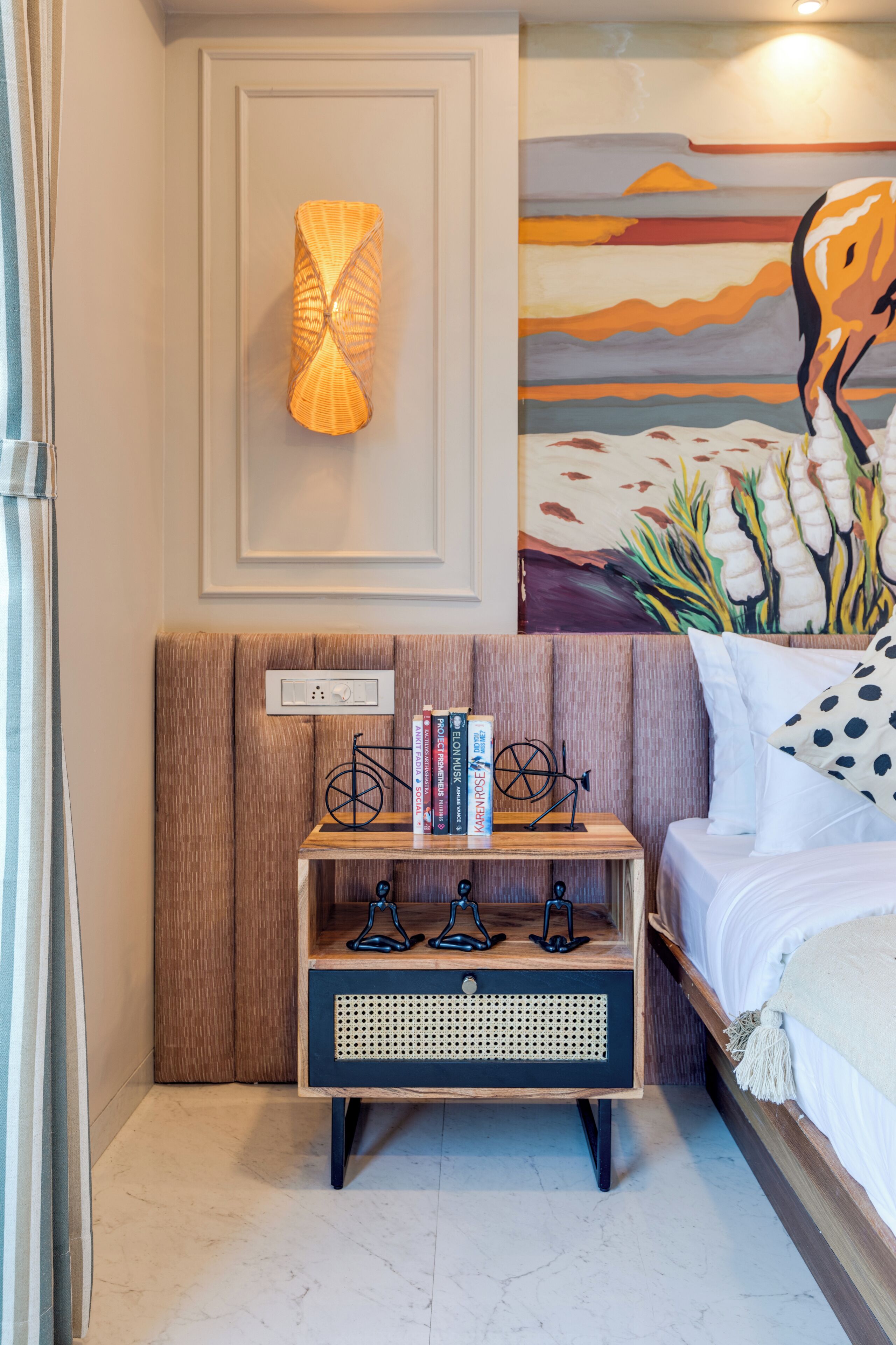 Un dormitorio con cama, una mesita de noche con libros, una lámpara de pared y un cuadro.