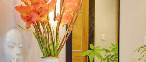 A wooden counter with a white vase containing orange flowers, a white bust sculpture, and a green plant.