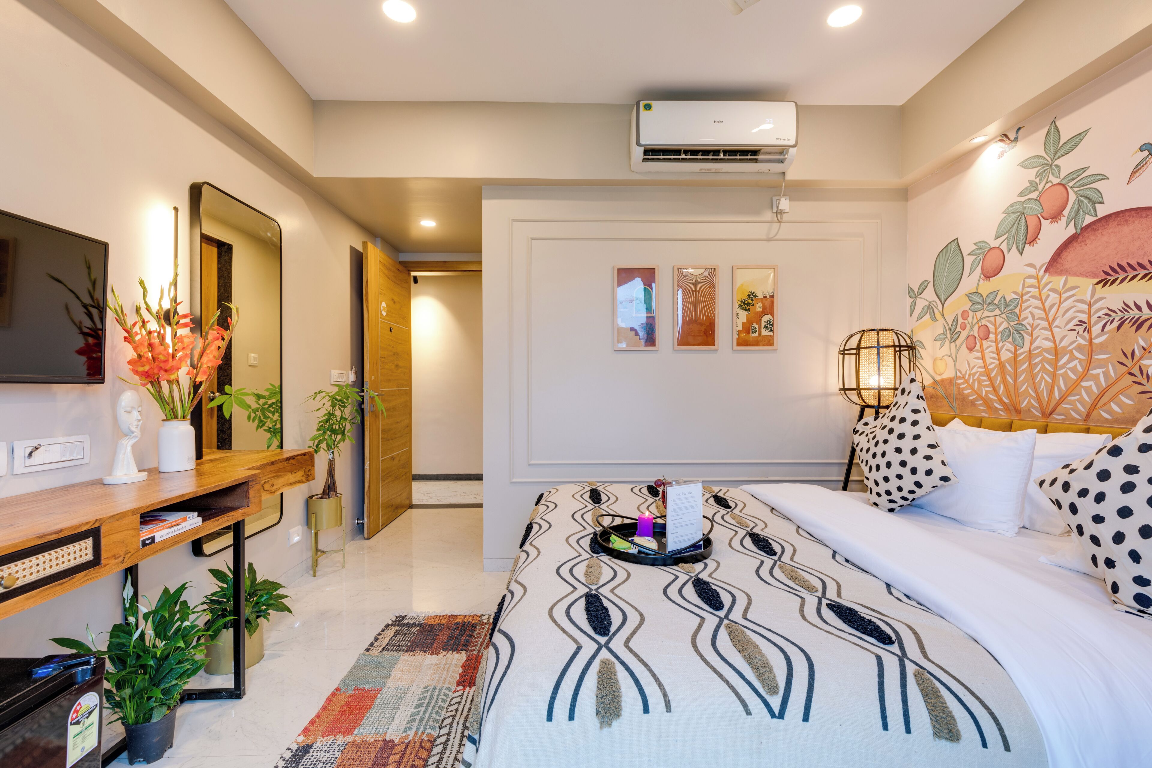 A hotel room with a bed, a desk with a computer, a mirror, and a wall-mounted air conditioner.