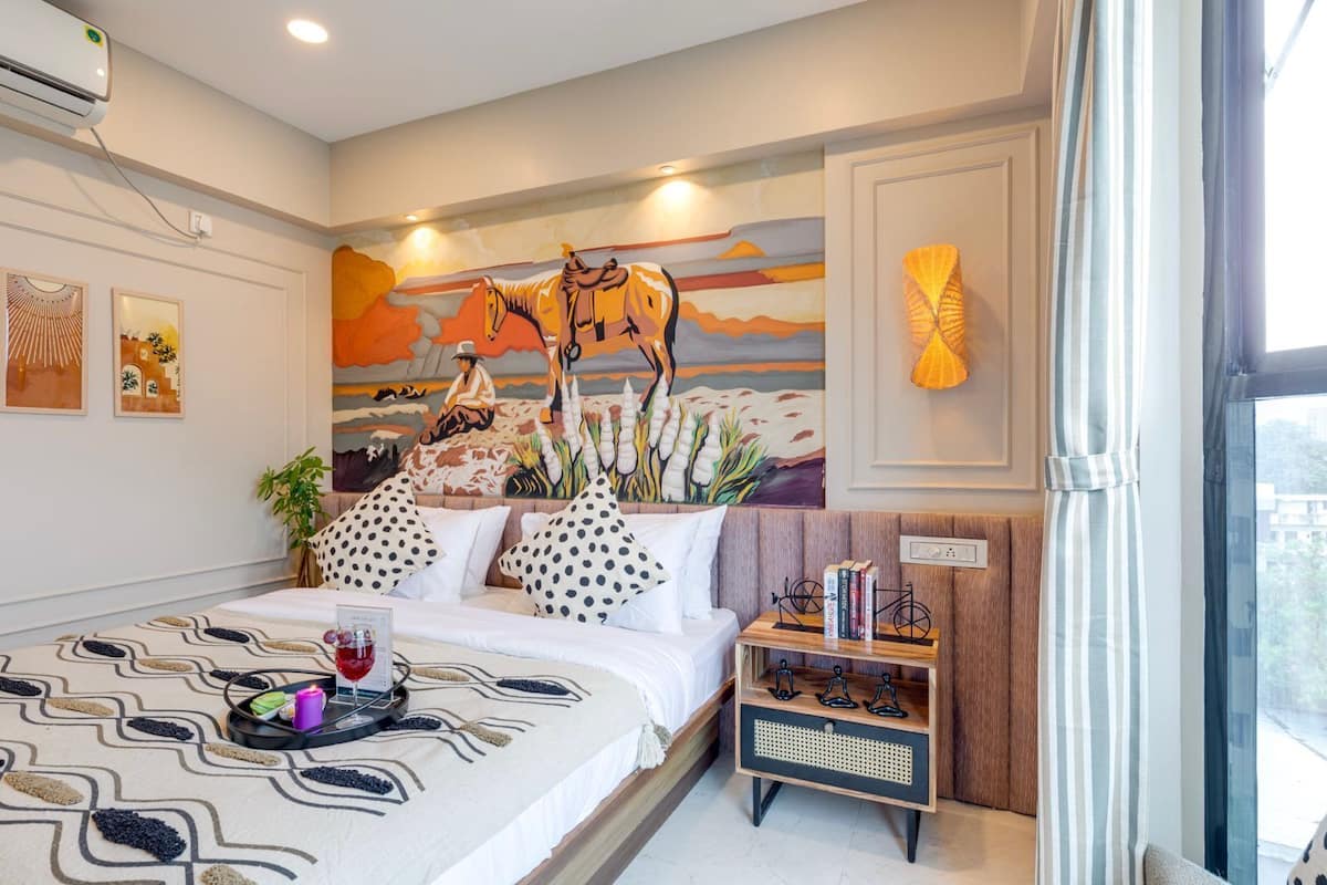 Une chambre à coucher moderne avec un grand lit, une fresque murale, une table de chevet avec des livres et une fenêtre avec des rideaux.