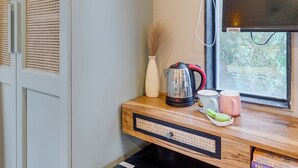 Una kitchenette compacta con refrigerador integrado, cafetera y un ventanal con vistas a la vegetación.