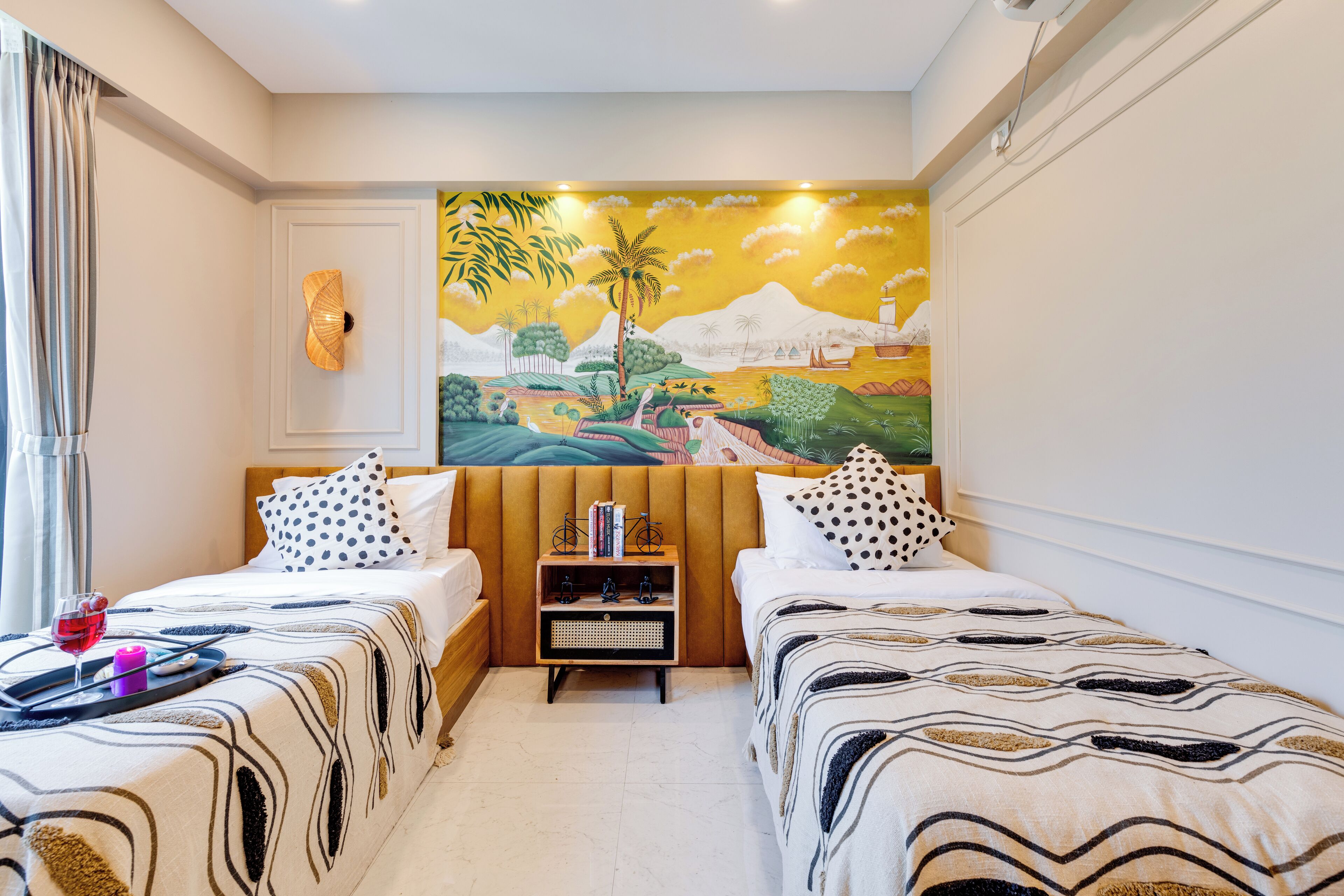 A hotel room with two beds, a painting on the wall, and a small table with books and a bicycle model.
