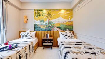 A hotel room with two beds, a painting on the wall, and a small table with books and a bicycle model.