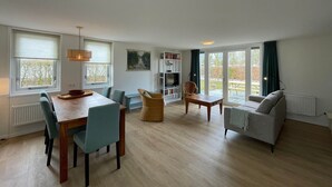 A spacious living area with a dining table, chairs, a sofa, and a bookshelf. - Chalet in Friesland Near Large Lakes (Sint Nicolaasga)