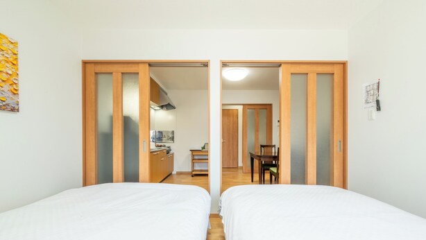 Een hotelkamer met twee bedden, een houten garderobe, een kitchenette en een eettafel.