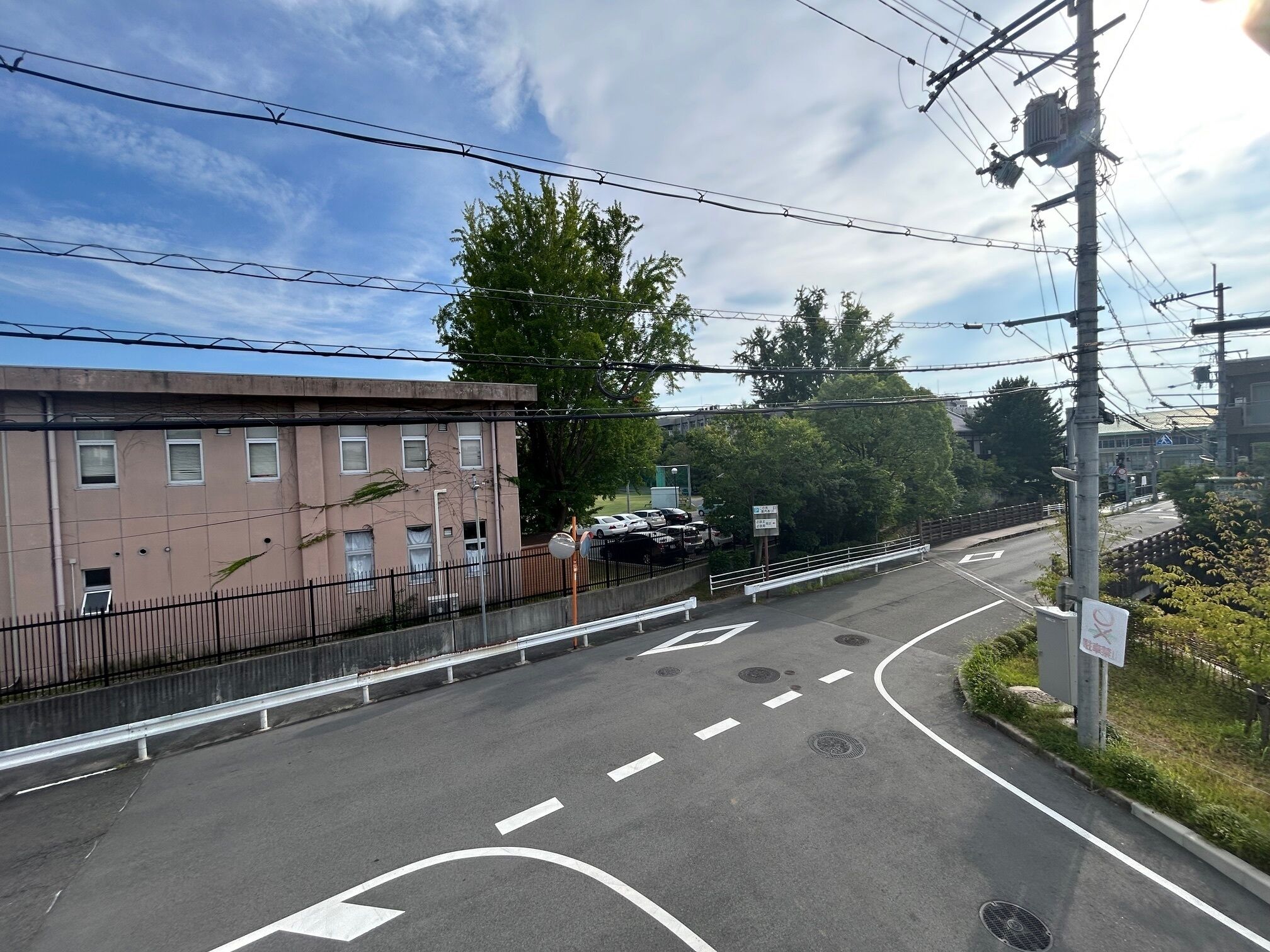 A multi-lane road with a pedestrian crossing, a fence, and a building with multiple windows.