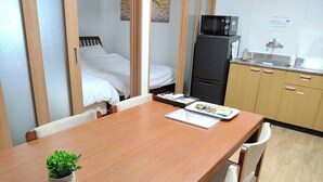 Hotelkamer met een houten eettafel, een kleine potplant, een bed met witte beddengoed, een zwarte koelkast, een magnetron, een wastafel en een kast.