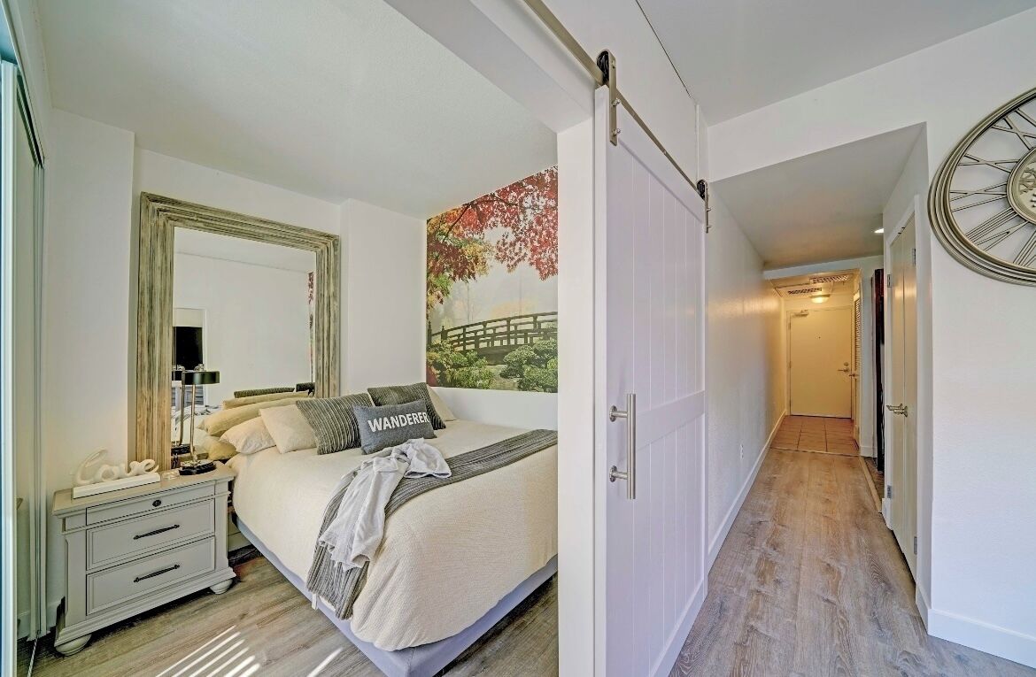 Un dormitorio con cama, mesita de noche y un espejo grande.