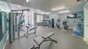 Un gimnasio con varios equipos de ejercicio, incluyendo cintas de correr, máquinas de pesas y una banca.