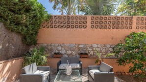 An outdoor patio with wicker furniture, a glass table, and potted plants. - 'Ideal Vacation Sun & Beach' Apartment with Private Pool, Terrace & Wi-Fi (Marbella)