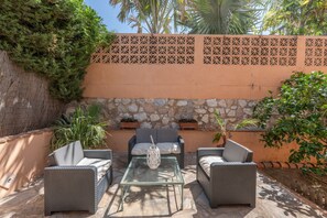 Une terrasse extérieure aménagée avec des meubles en osier, une table en verre et des plantes en pot.