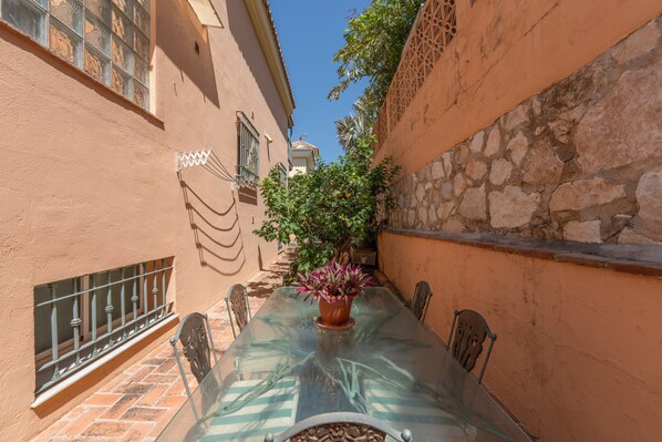 Une ruelle étroite avec une table et des chaises en verre, une plante en pot et un mur de pierre.