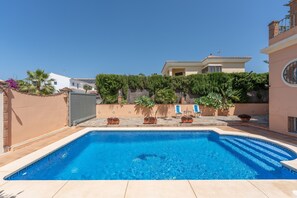 Une piscine dotée d’une terrasse carrelée, entourée de plantes en pot et bordée d’un bâtiment dont le toit est également recouvert de tuiles.