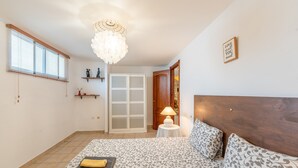 A bedroom with a bed, a chandelier, a door, a small table with a lamp, and a shelf with decorative items. - 'Ideal Vacation Sun & Beach' Apartment with Private Pool, Terrace & Wi-Fi (Marbella)