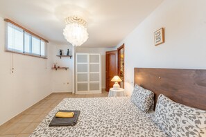 Une chambre Ă coucher comprenant un lit, un lustre, une porte, une petite table avec une lampe et une Ă©tagĂšre ornĂ©e dâobjets dĂ©coratifs.