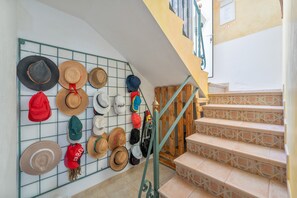 Un escalier avec un mur en forme de grille oĂč sont exposĂ©s diffĂ©rents chapeaux.