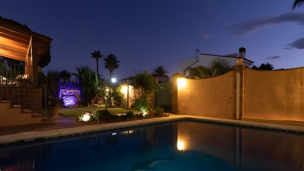 A swimming pool with a clear view of the water, a wooden deck, and a well-lit outdoor area with plants and a small waterfall feature. - 'Ideal Vacation Sun & Beach' Apartment with Private Pool, Terrace & Wi-Fi (Marbella)