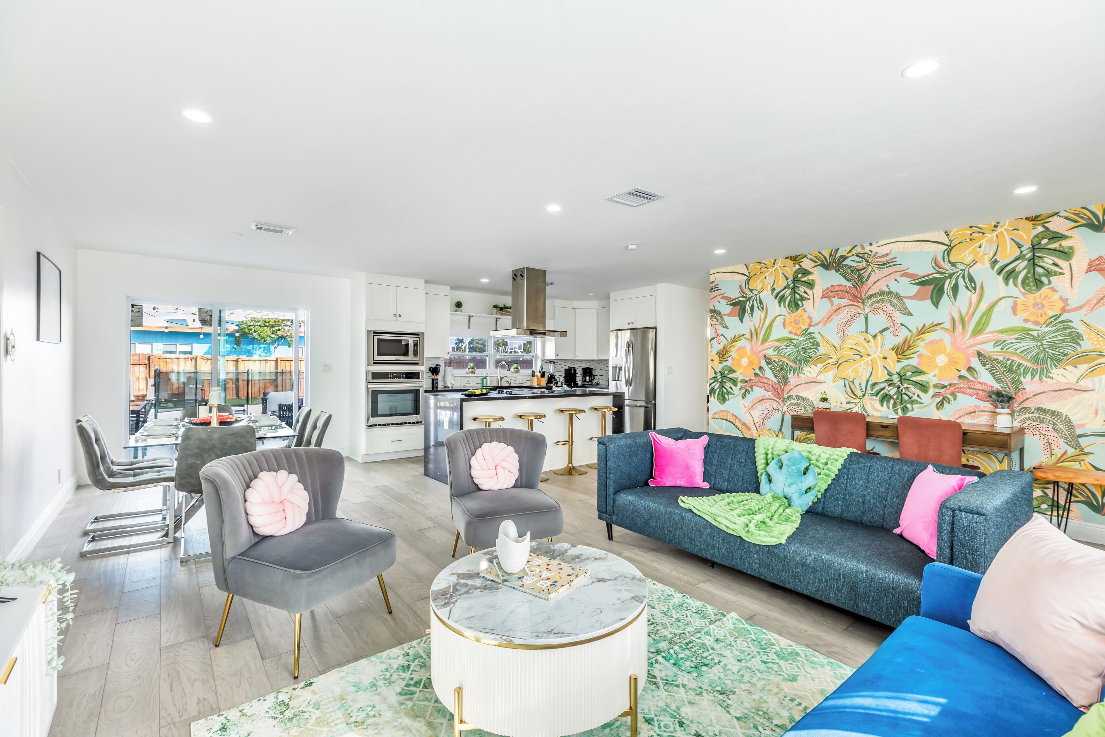 A modern living room with a grey sofa, a round coffee table, and a vibrant tropical wallpaper.