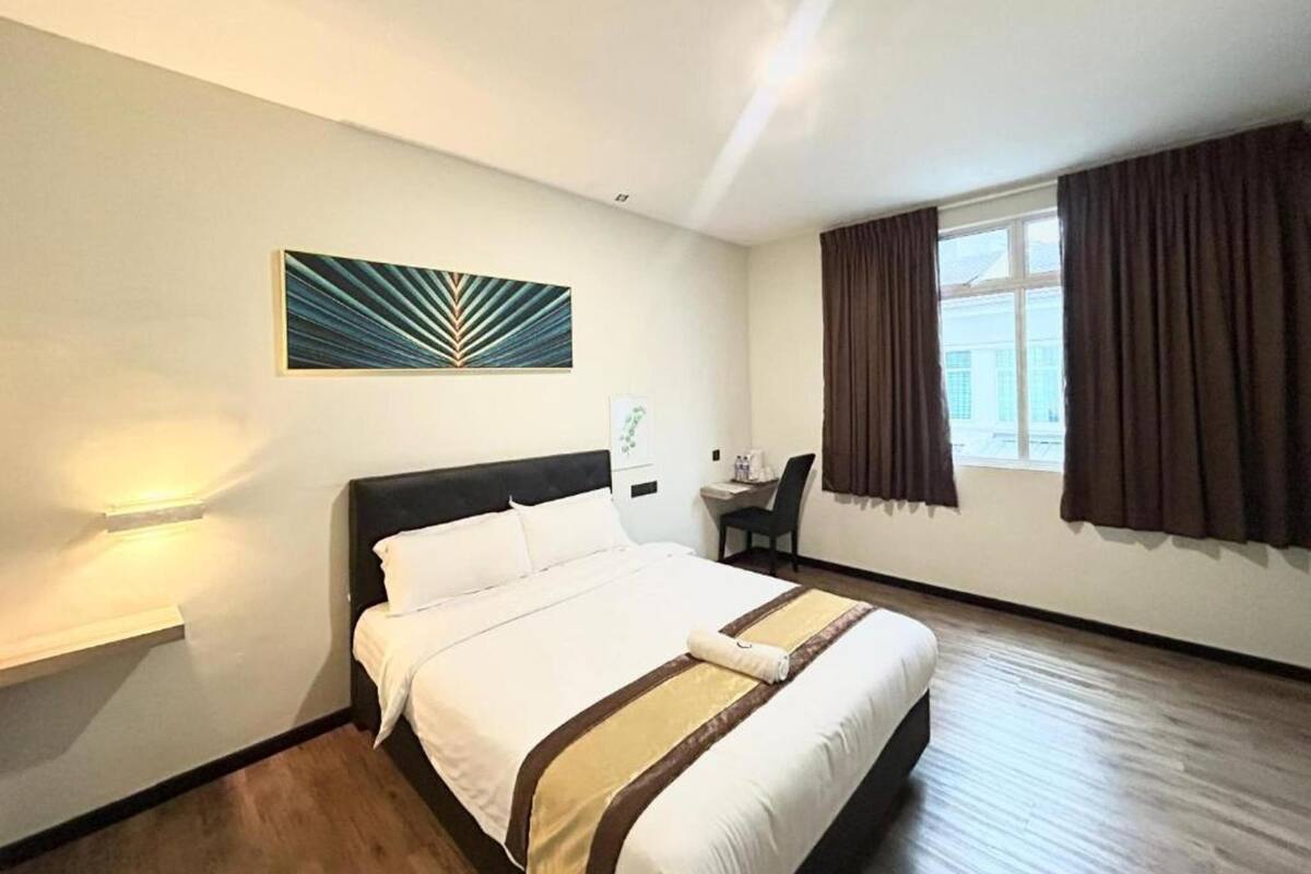 Une chambre d’hôtel comprenant un lit, un bureau, une chaise, une fenêtre avec des rideaux et une œuvre d’art accrochée au mur.