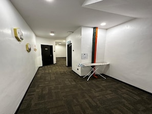 A hallway with a carpeted floor, white walls, a black door, and a wall-mounted ironing board. - Gill Garden Boutique Hotel (Malacca City)