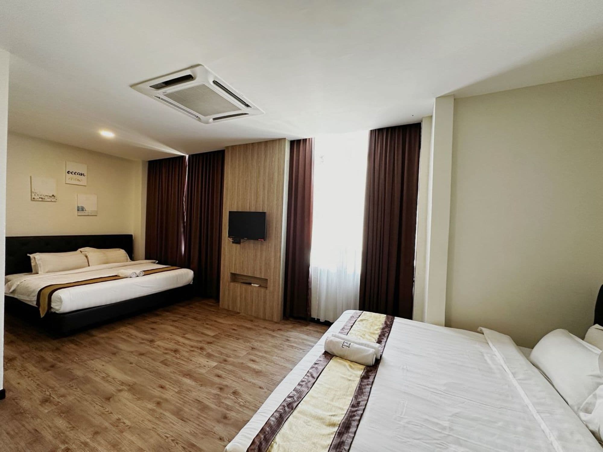 A hotel room with two beds, a flat-screen TV, wooden flooring, and a large window with curtains.